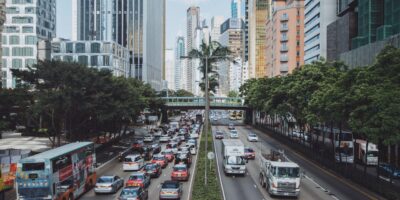 case studies image - a cityscape background nests a large highway with greenery on either side. There are many cars heading into the city, and fewer cars leaving the city. In the middle of the directions, there's a median with greenery and large palm trees. A beautiful blue sky with clouds can be seen in the background behind all the tall skyscrapers.
