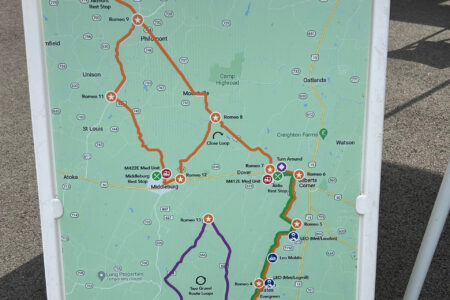 An image of a large plastic floor sign that holds a map with many routes on it. There's one that is the largest in orange, and one that sticks out in purple coloring. The rest of the map is green and looks like a Google Maps image.