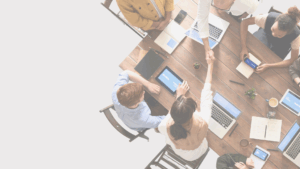 a group of people sit around a wooden table and look to be making an agreement. there are wooden chairs and the view is from the top-down.