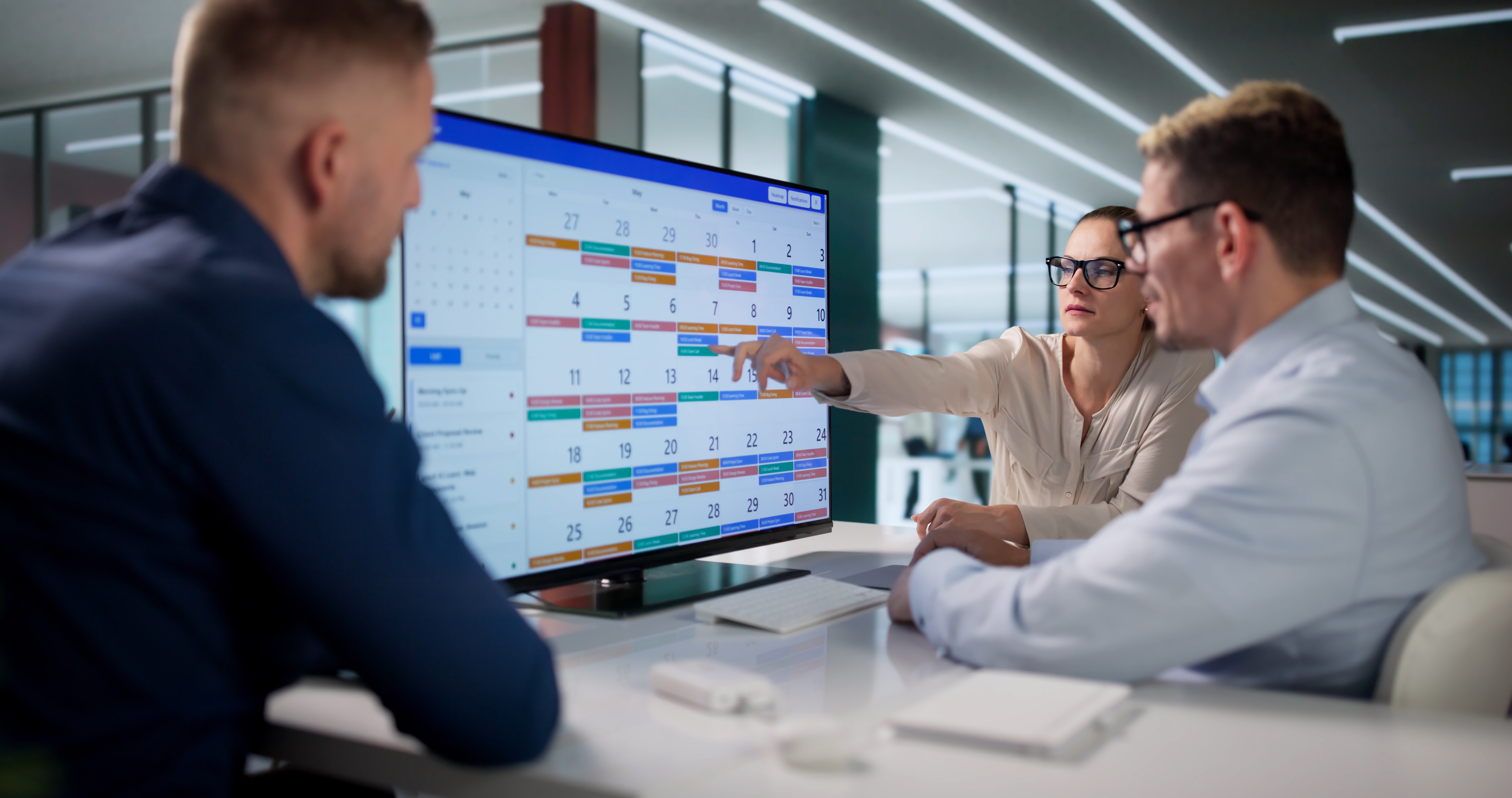 Project team reviewing a project management schedule and timeline on a digital display during a planning meeting.